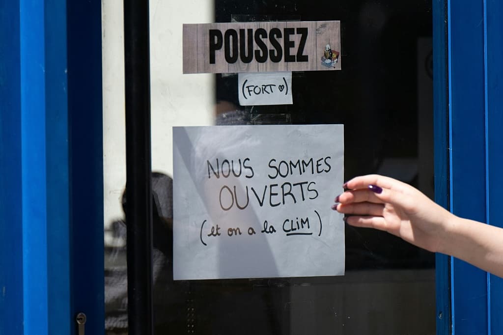 A sign reading in French "We are open and we have air conditioning" is displayed outside a business