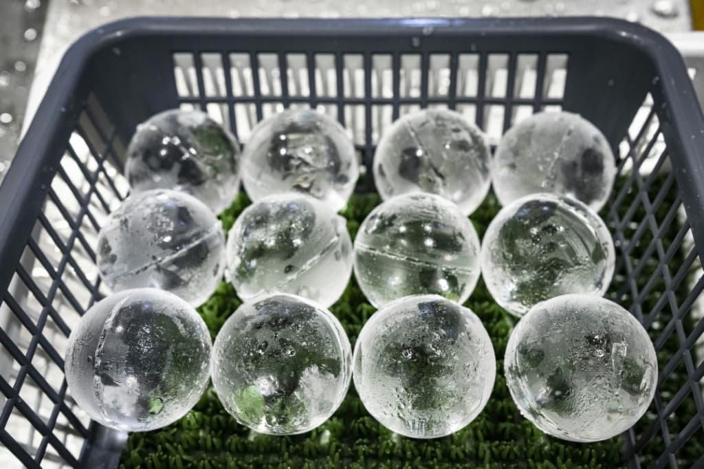 workers haul large blocks of ice across the factory floor, before starting on the delicate work of carving perfect spheres, cubes and rectangular blocks with cut corners