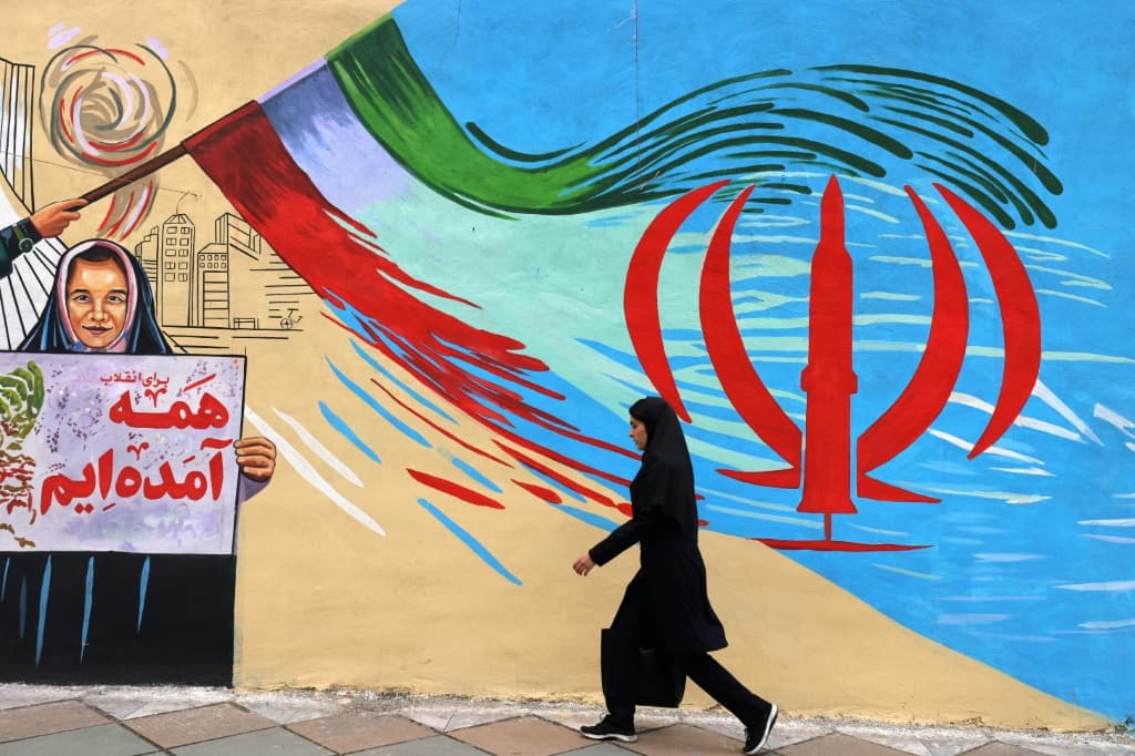 An Iranian woman walks past an anti-US and anti-Israel mural in Tehran