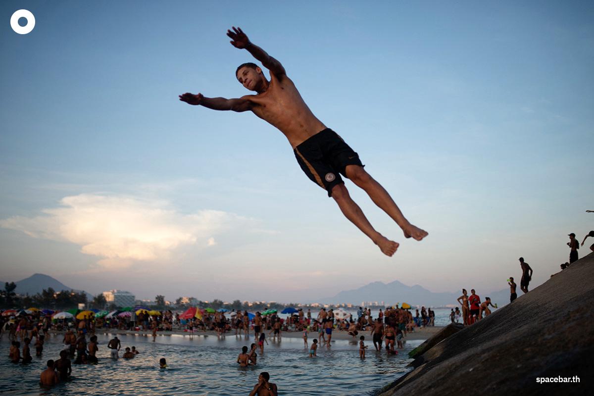 วัยรุ่นชายคนหนึ่งกำลังกระโดดลงน้ำทะเลจากโขดหินที่ชายหาดเรเซอีโอ โดส บันเดรันเตส (Recreio dos Bandeirantes) ท่ามกลางคลื่นความร้อนในเมืองรีโอเดจาเนโร ประเทศบราซิล เมื่อวันที่ 17 มีนาคม 2024 (Photo by TERCIO TEIXEIRA / AFP) 