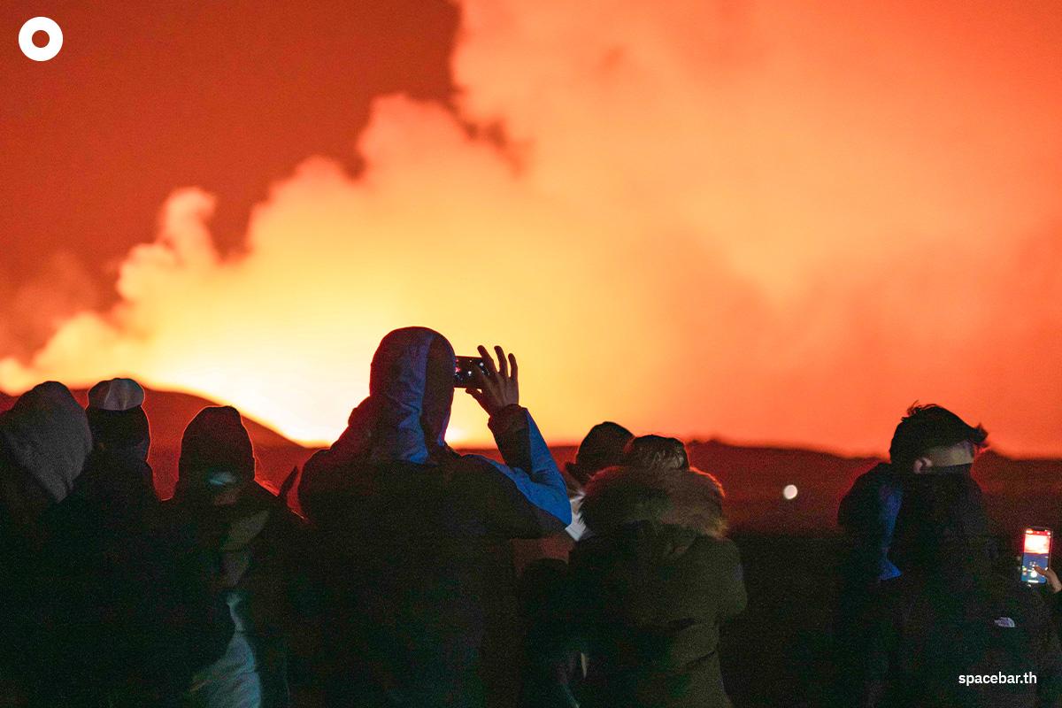 ผู้คนกำลังดูลาวาไหลออกมาจากรอยแยกบนคาบสมุทรเรคยาเนส ทางเหนือของเมืองกวินดาวิก ซึ่งอยู่ทางตะวันตกของไอซ์แลนด์ เมื่อวันที่ 16 มีนาคม 2024 (Photo by Ael Kermarec / AFP) 